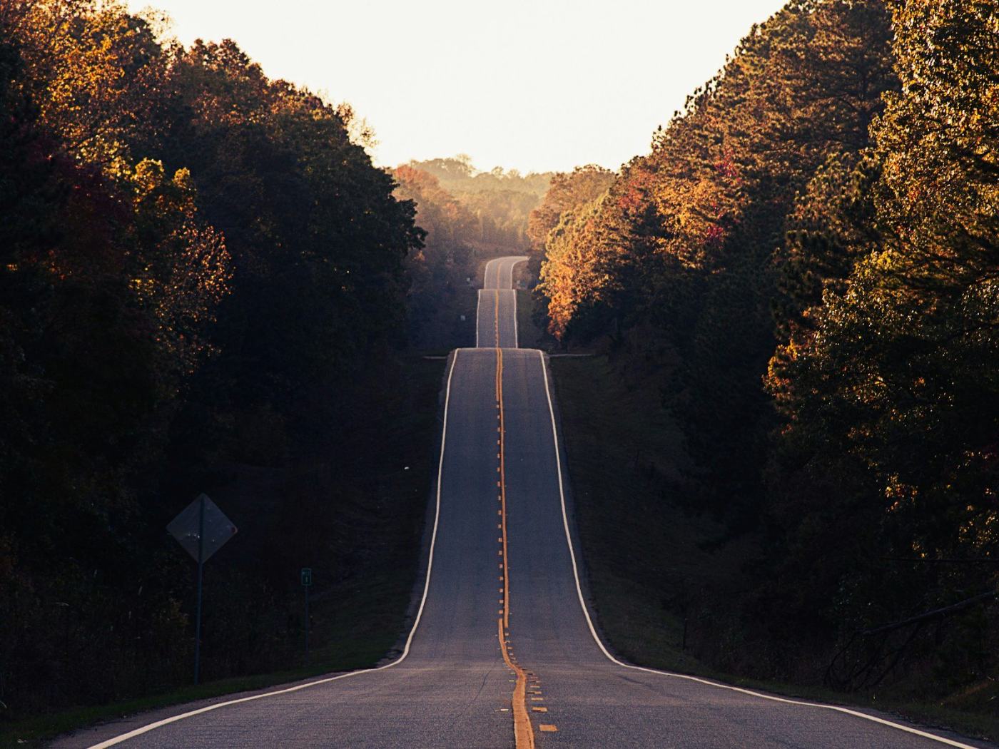 A long road rising and falling through wooded hills at sunset.