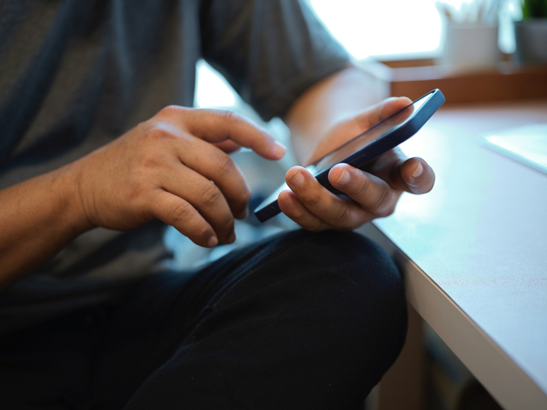A pair of hands holding a phone at a desk, waiting.