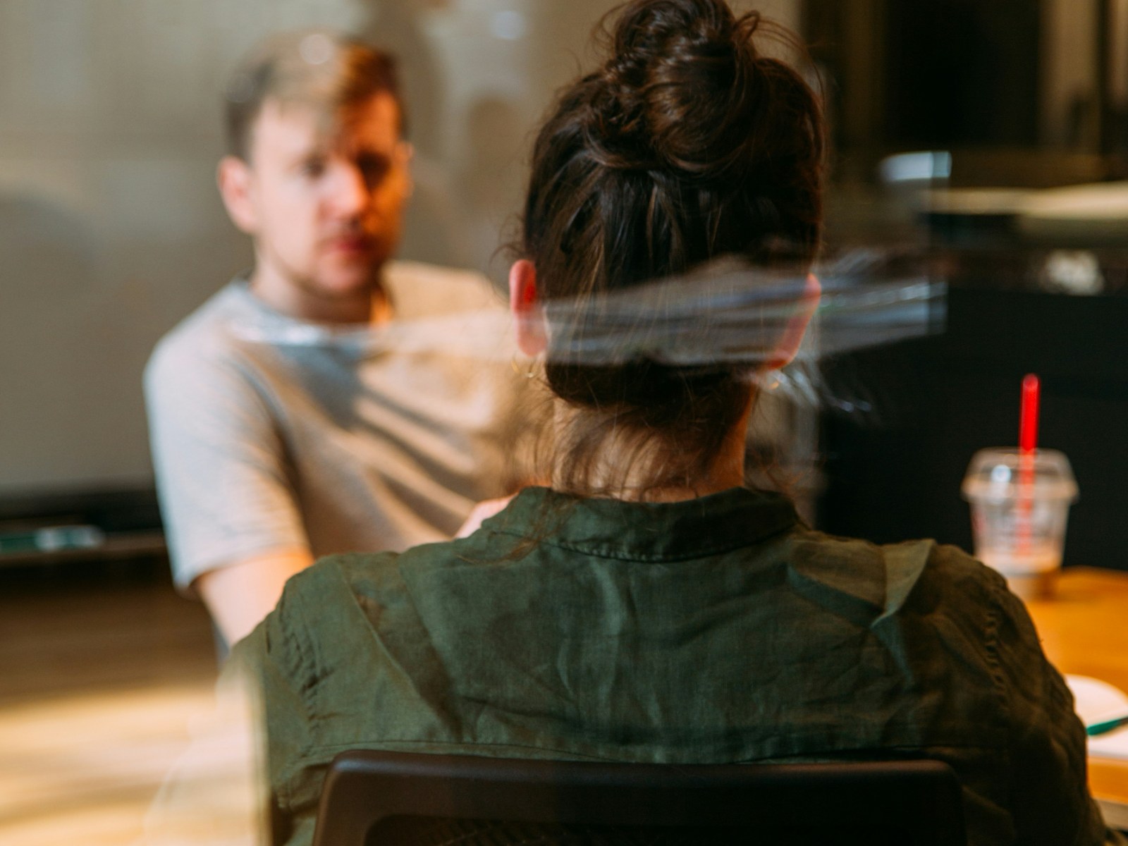 Two people talking across a table in a meeting room, seen through glass.