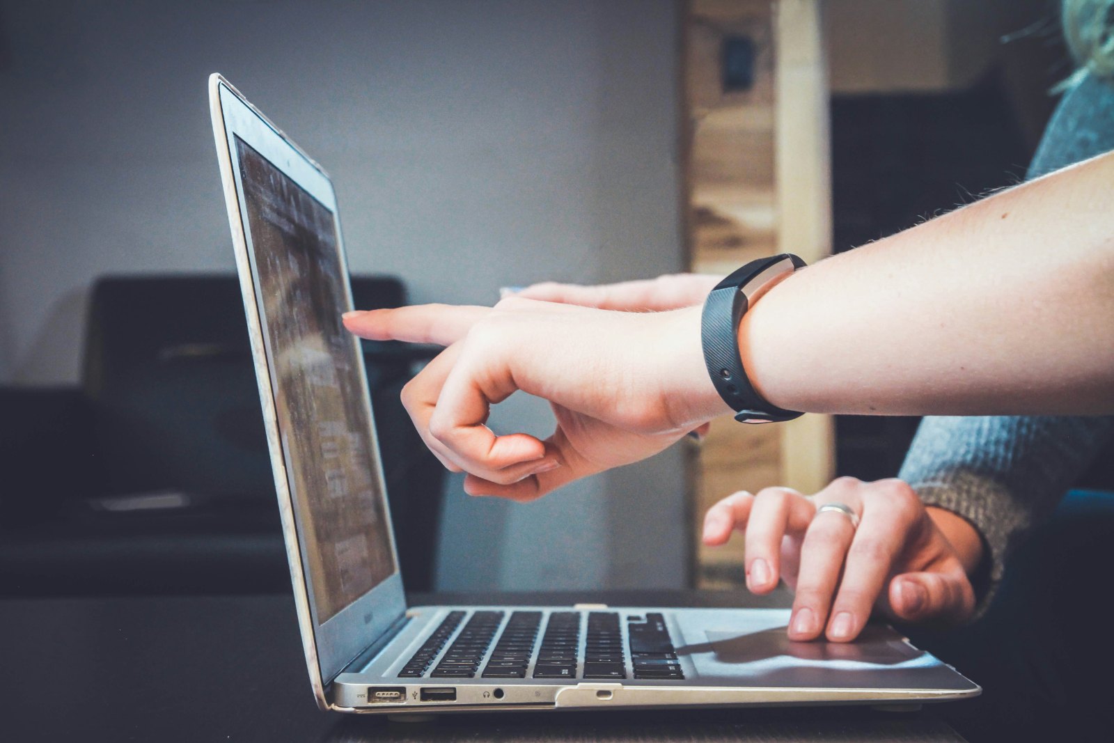 Two people at a laptop, one pointing at the screen while the other works the trackpad.