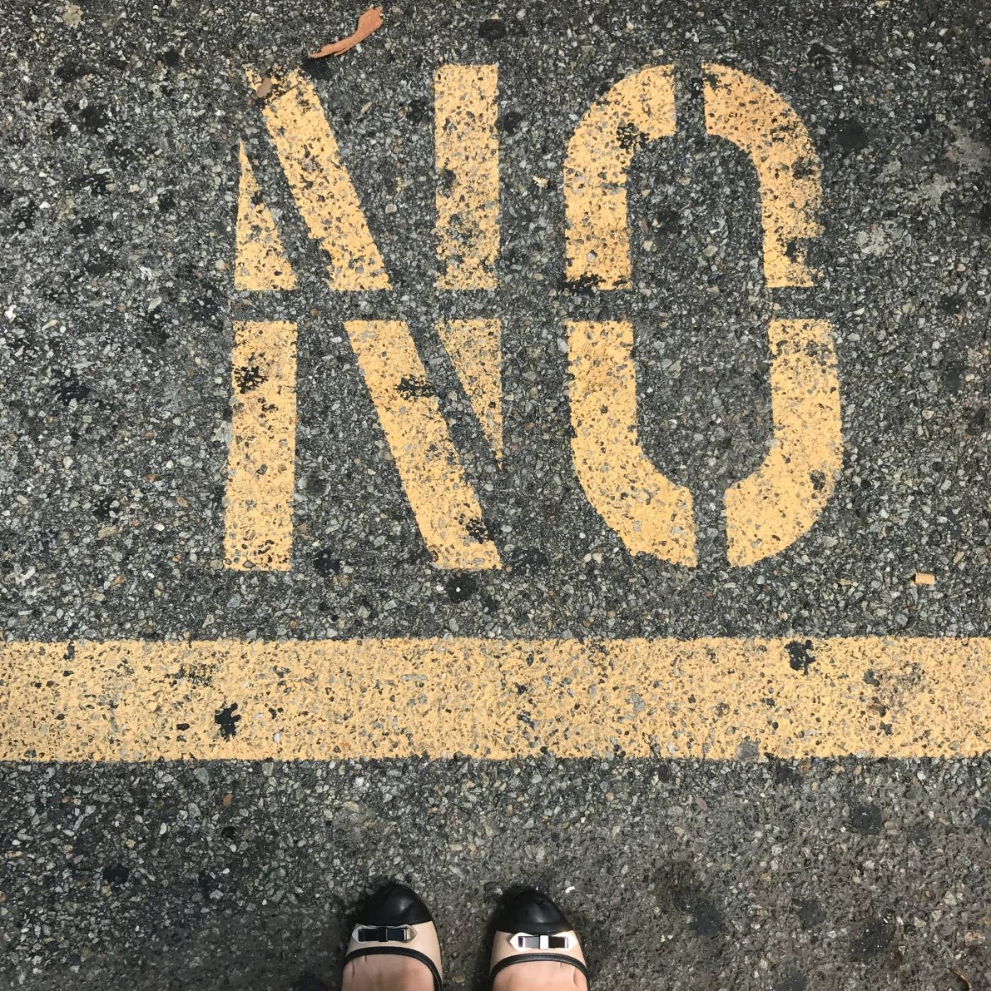 The word NO stencilled in yellow paint on tarmac, seen from above.