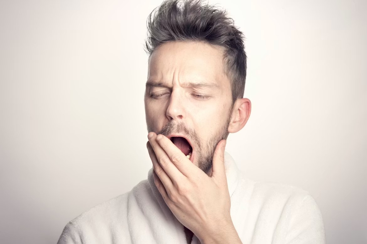 A man in a white robe yawning with his hand over his mouth.